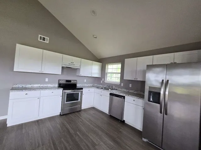 a kitchen with stainless steel appliances granite countertop a stove a sink dishwasher a refrigerator and white cabinets with wooden floor