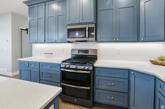 1009 High Creek Road Cove, UT 84320 - Photo 20 of 79 Kitchen featuring stainless steel appliances, blue cabinetry, light stone counters, and tasteful backsplash