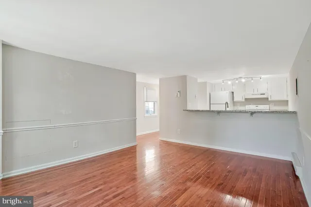 a view of an empty room with wooden floor and kitchen