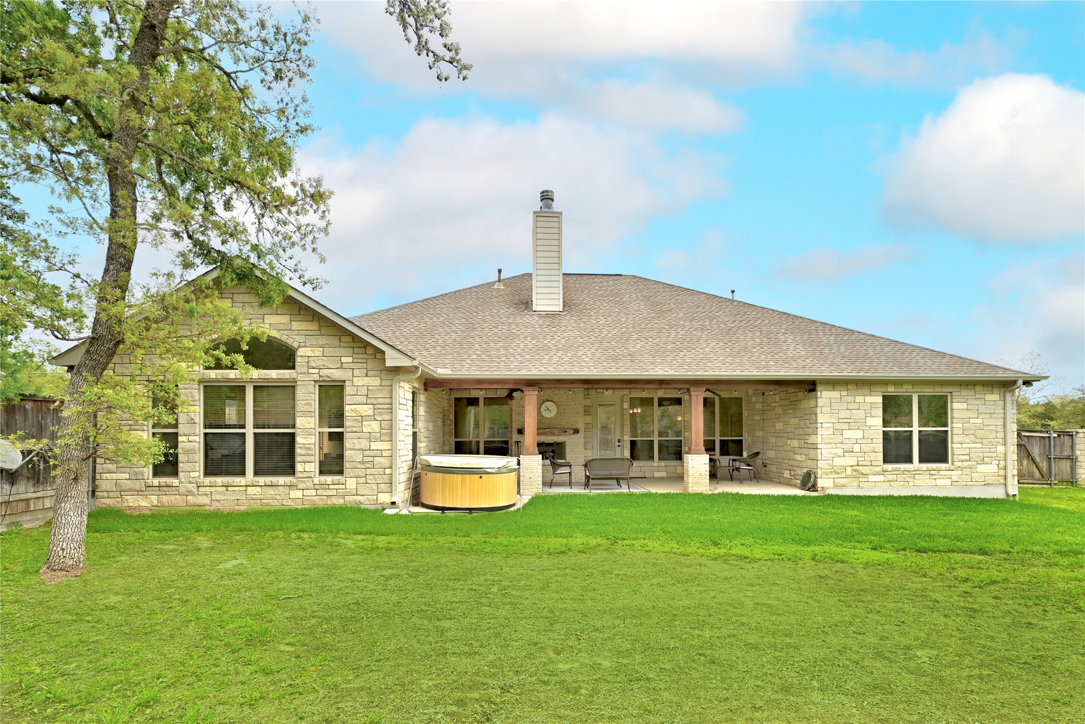 140 Winchester Road Bastrop, TX 78602 - Photo 31 of 35 Rear view of house with stone siding, a hot tub, a fenced backyard, a patio area, and a chimney