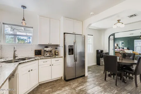 a kitchen with stainless steel appliances granite countertop a refrigerator a sink dishwasher a stove and white cabinets with wooden floor