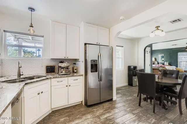 a kitchen with stainless steel appliances granite countertop a refrigerator a sink dishwasher a stove and white cabinets with wooden floor