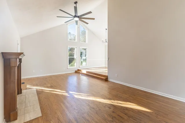 an empty room with wooden floor chandelier fan and windows