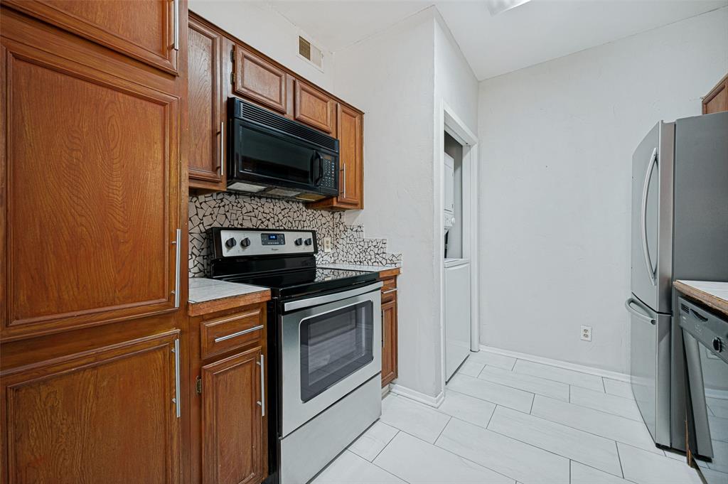 5550 Spring Valley Road, Unit C21 Dallas, TX 75254 - Photo 12 of 26 Wood cabinetry, mosaic tile backsplash, black over-the-range microwave, stainless steel range, and light-toned tile flooring