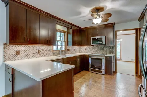 a large kitchen with stainless steel appliances granite countertop a refrigerator a sink dishwasher a stove and white countertops with wooden floor
