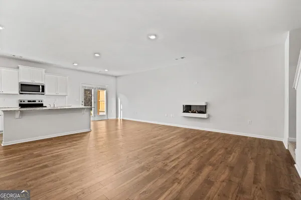 a view of empty room with wooden floor and kitchen view