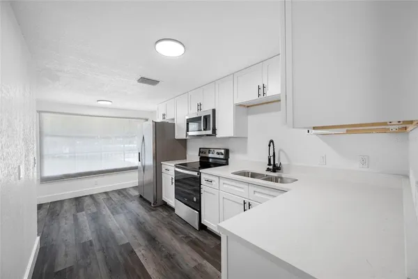 a kitchen that has a microwave a stove and white cabinets with wooden floor