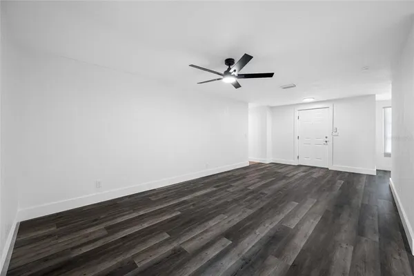 a view of an empty room with wooden floor and a ceiling fan