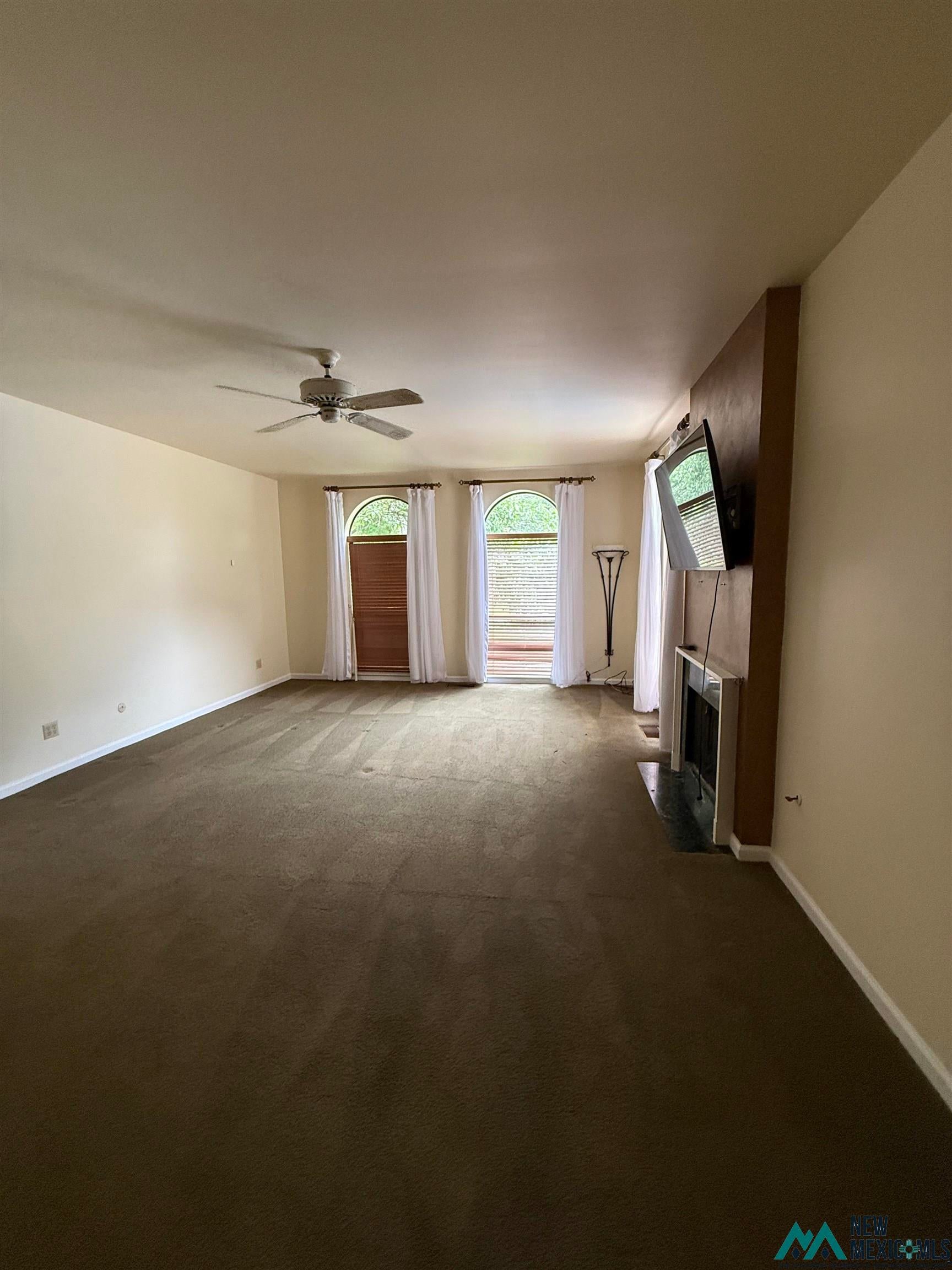 1111 West Country Road Roswell, NM 88201 - Photo 30 of 41 Spacious living area featuring neutral carpeting, a ceiling fan with integrated lighting, and a prominent fireplace with a dark stone hearth