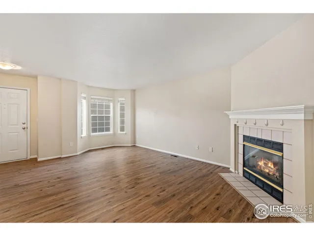 a view of an empty room with wooden floor fireplace and a window