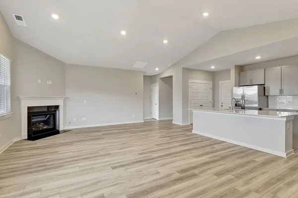 a view of an empty room with wooden floor and a kitchen