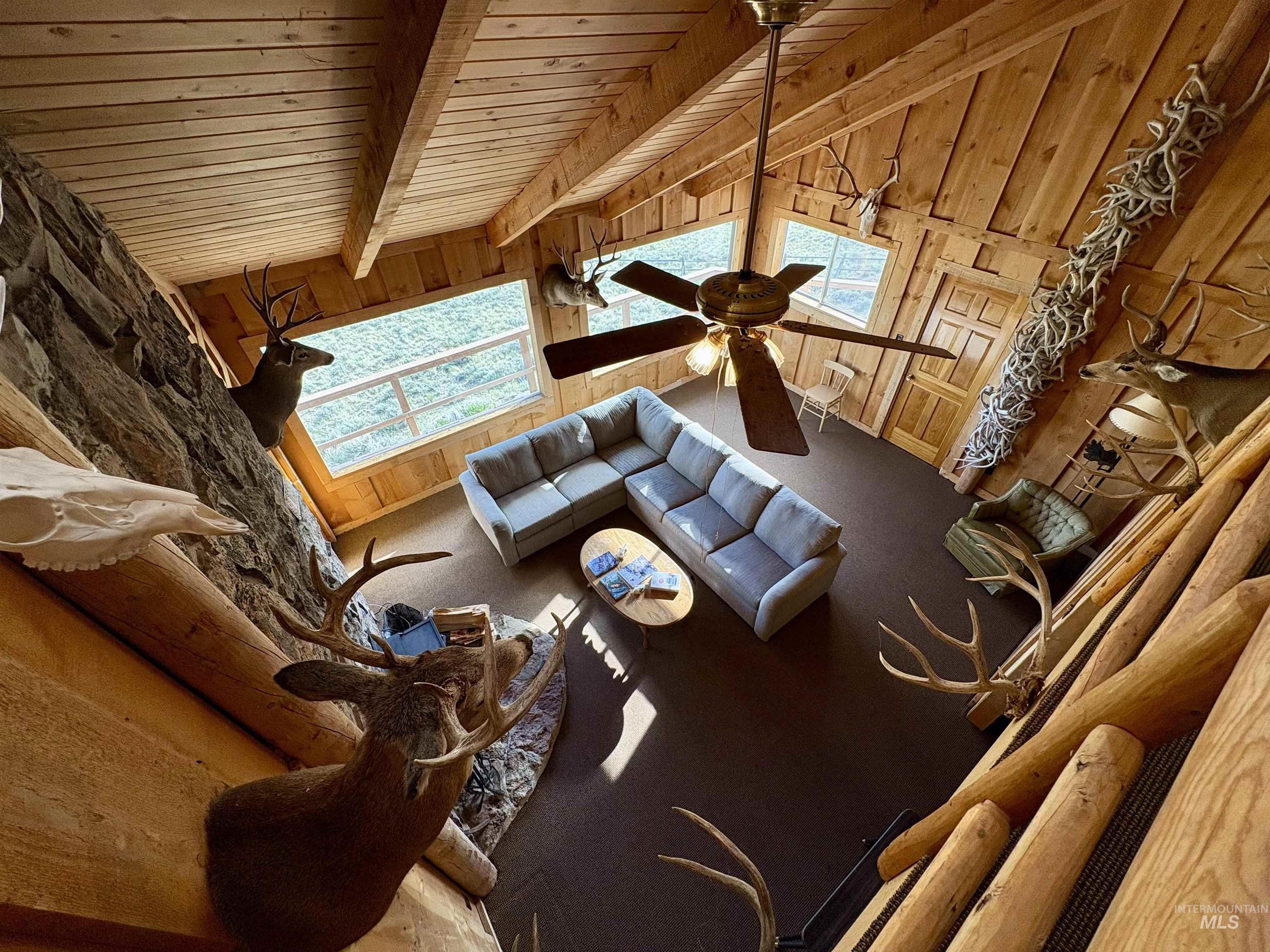 2040 Pahsimeroi River Road May, ID 83253 - Photo 21 of 29 Vaulted wood plank ceiling with exposed beams, stone accent wall, wood-finish flooring, large picture window, and ceiling fan with integrated lighting