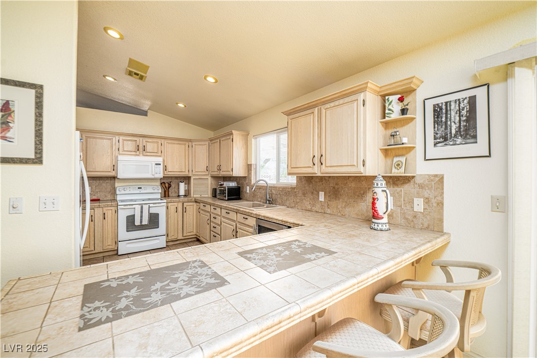 475 East Robindale Road Las Vegas, NV 89123 - Photo 8 of 41 Kitchen with white appliances, light brown cabinetry, lofted ceiling, backsplash, and a sink