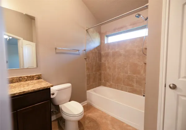 a bathroom with a granite countertop bathtub shower sink vanity and toilet