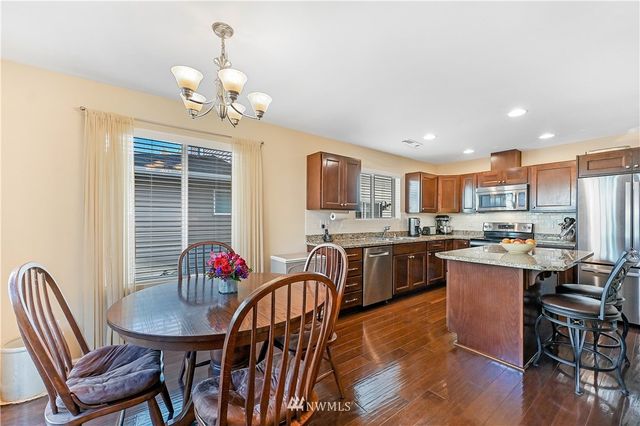a open dining room with stainless steel appliances kitchen island granite countertop a dining table chairs kitchen island with wooden floor and cabinets