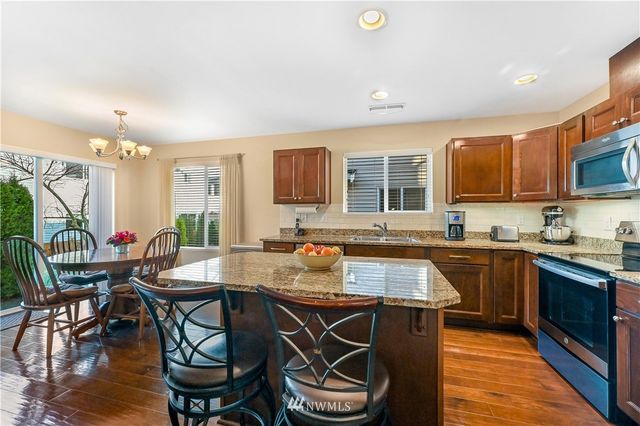 a kitchen with stainless steel appliances granite countertop wooden cabinets a stove a sink a dining table and chairs