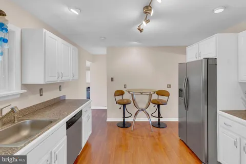 a kitchen with stainless steel appliances granite countertop a refrigerator a sink a stove and white cabinets with wooden floor