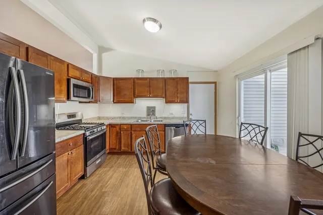 a kitchen with stainless steel appliances granite countertop a stove a refrigerator a kitchen island a table and chairs with wooden floor