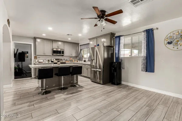 a kitchen with stainless steel appliances kitchen island granite countertop a refrigerator a stove top oven and a sink with wooden floor