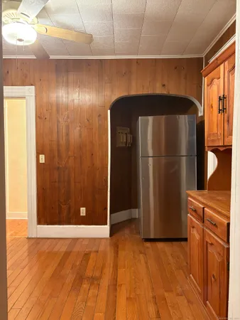 a view of a refrigerator in kitchen and an empty room with wooden floor