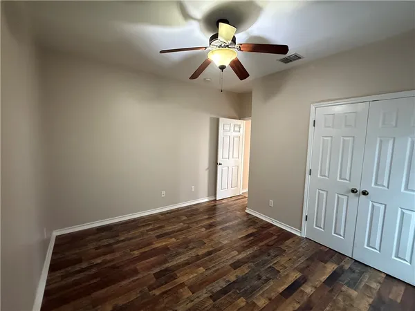a view of an empty room with wooden floor and a ceiling fan