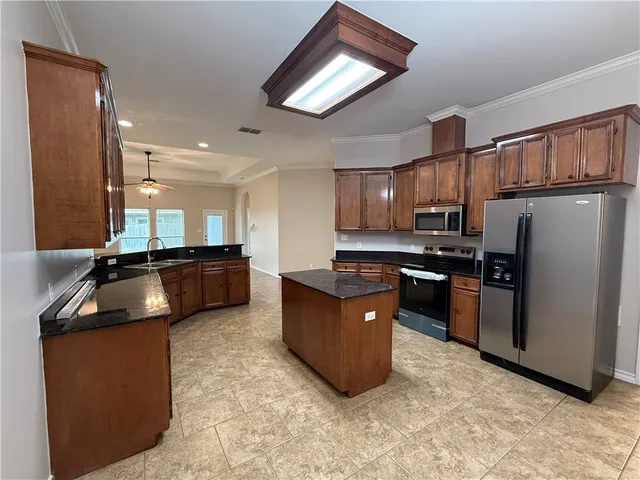 a kitchen with stainless steel appliances kitchen island granite countertop a refrigerator a sink a stove a microwave oven and a dining table with wooden floor