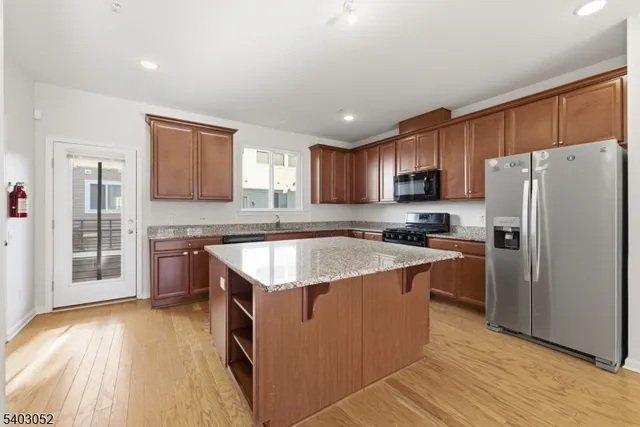 a kitchen with stainless steel appliances granite countertop a refrigerator a sink dishwasher a stove with wooden cabinets and floors