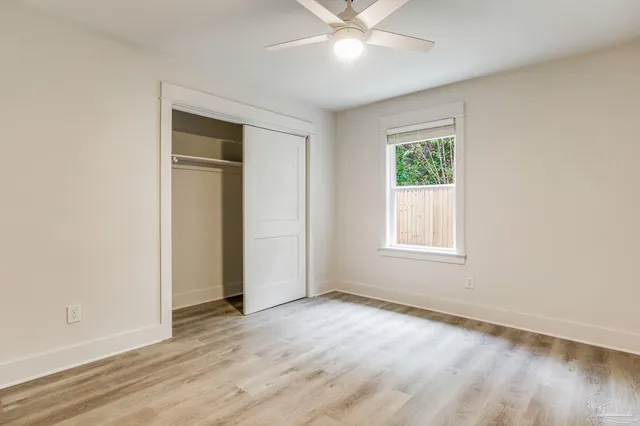 an empty room with wooden floor fan and windows