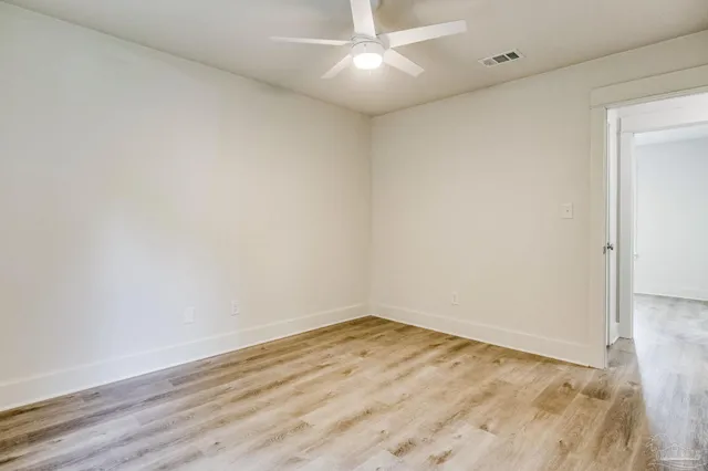 an empty room with wooden floor and fan