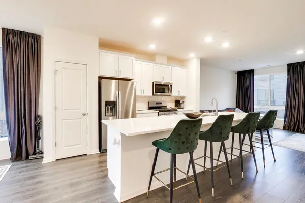 a kitchen with stainless steel appliances granite countertop a stove a refrigerator a microwave a dining table and chairs with wooden floor