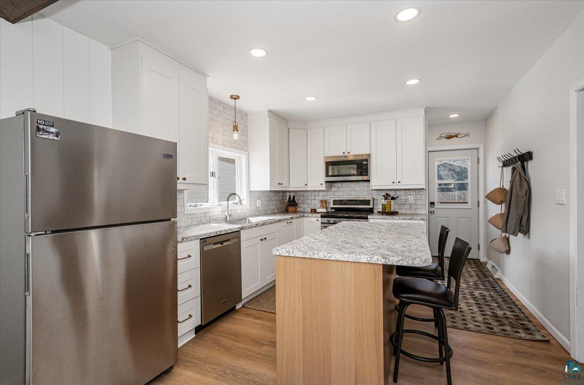 415 14th Street Cloquet, MN 55720 - Photo 2 of 20 Kitchen with stainless steel appliances, a kitchen island, a breakfast bar area, dark wood-type flooring, and decorative backsplash