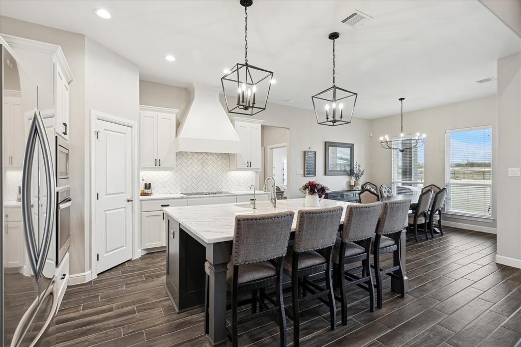 112 Friendship Way Boyd, TX 76023 - Photo 9 of 29 Open-concept kitchen featuring an oversized island with seating, white shaker cabinetry, stainless steel appliances, and a herringbone tile backsplash