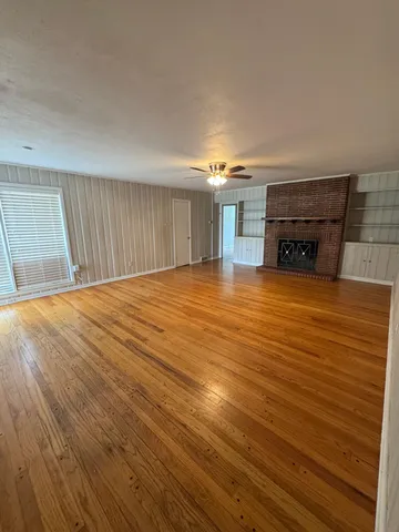 a view of an empty room with wooden floor fireplace and a window