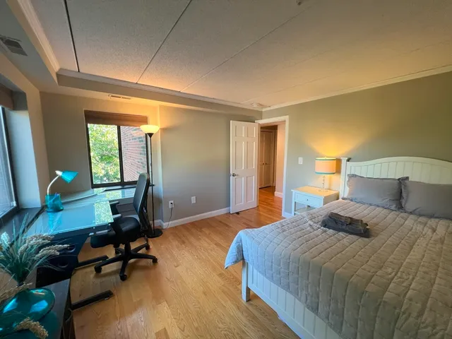 a bedroom with a bed a desk and chair with wooden floor