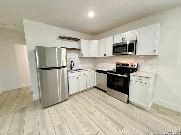 a kitchen with stainless steel appliances granite countertop white cabinets a sink a stove a refrigerator and a microwave
