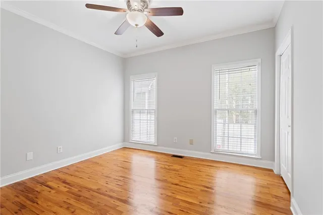 an empty room with wooden floor chandelier fan and windows