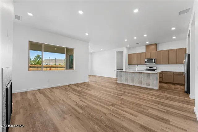 a view of kitchen with kitchen island granite countertop wooden floor stainless steel appliances and a window