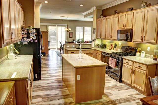 a kitchen with stainless steel appliances granite countertop a stove top oven a sink dishwasher and a refrigerator with wooden floor