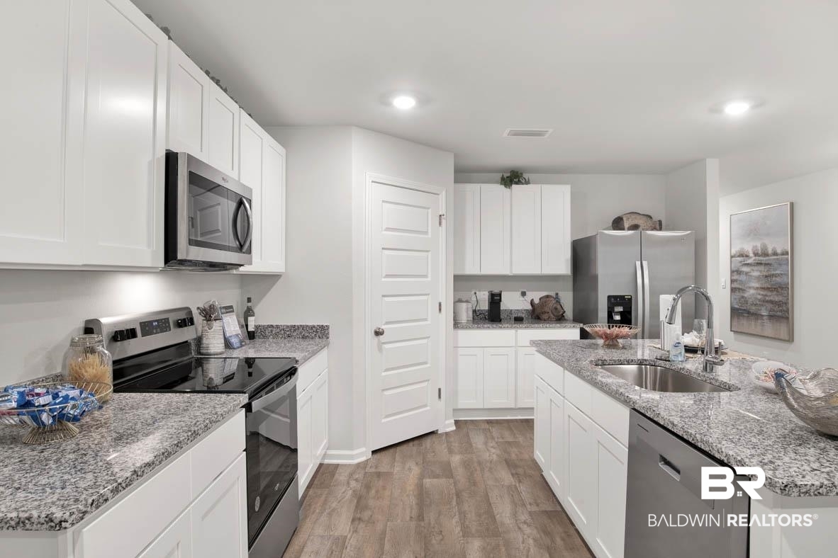 1235 Hayward Loop Foley, AL 36535 - Photo 13 of 26 Kitchen with light hardwood / wood-style flooring, appliances with stainless steel finishes, an island with sink, sink, and white cabinetry