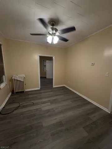 a view of an empty room with wooden floor and a ceiling fan