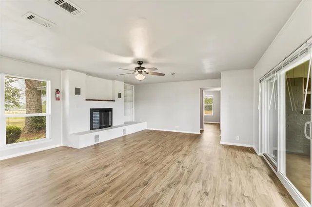 a view of an empty room with wooden floor fireplace and a window