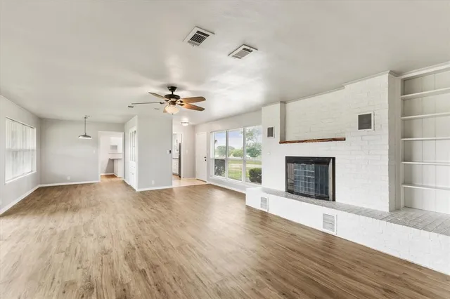 a view of an empty room with wooden floor fireplace and a window