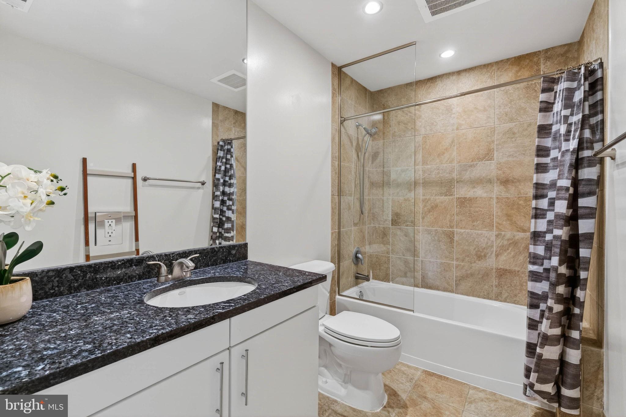 3409 Wilson Boulevard, Unit 301 Arlington, VA 22201 - Photo 25 of 39 a bathroom with a granite countertop sink a toilet a mirror a vanity and bathtub