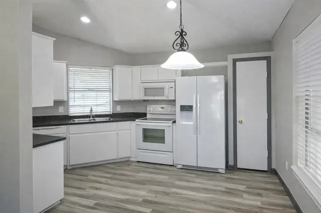 an empty room with wooden floor chandelier fan and windows