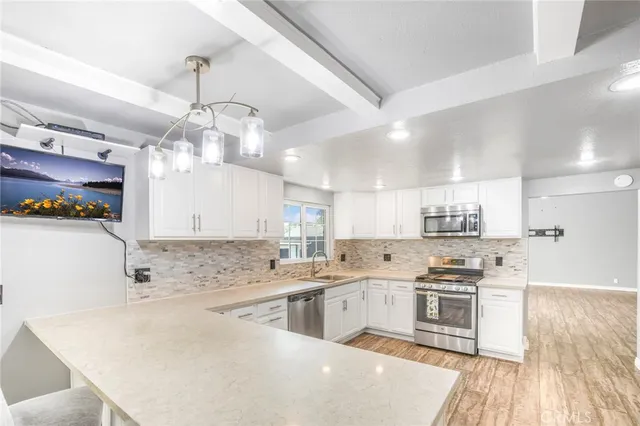 a kitchen with stainless steel appliances kitchen island granite countertop a sink a stove a refrigerator cabinets and chairs with wooden floor