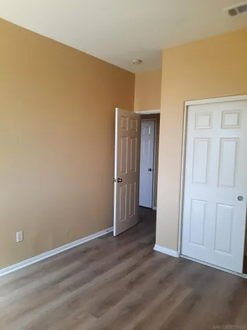 a view of an empty room with wooden floor and closet