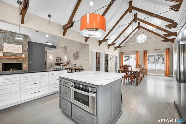 a kitchen with stainless steel appliances a stove a chimney a dining table and chairs with wooden floor