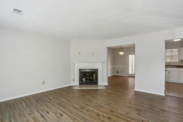 a view of an empty room with wooden floor fireplace and a window