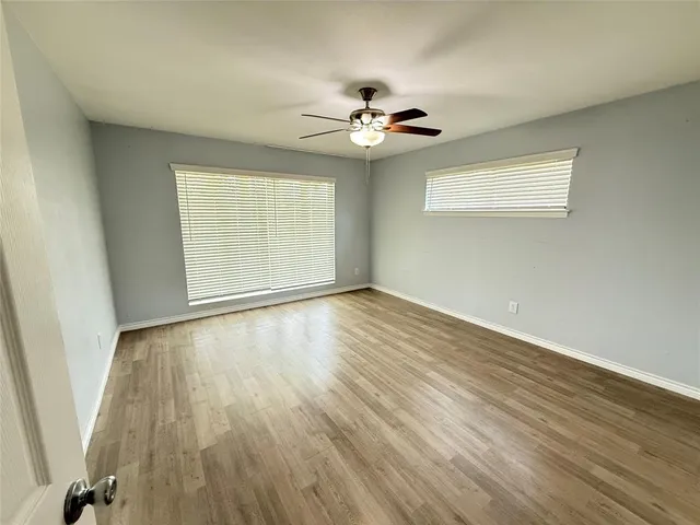an empty room with wooden floor chandelier fan and windows