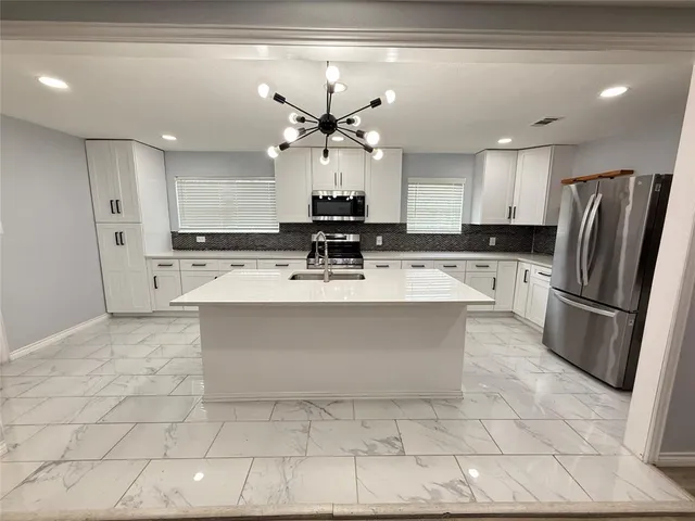 a kitchen with stainless steel appliances a sink a stove a refrigerator cabinets and a dining table